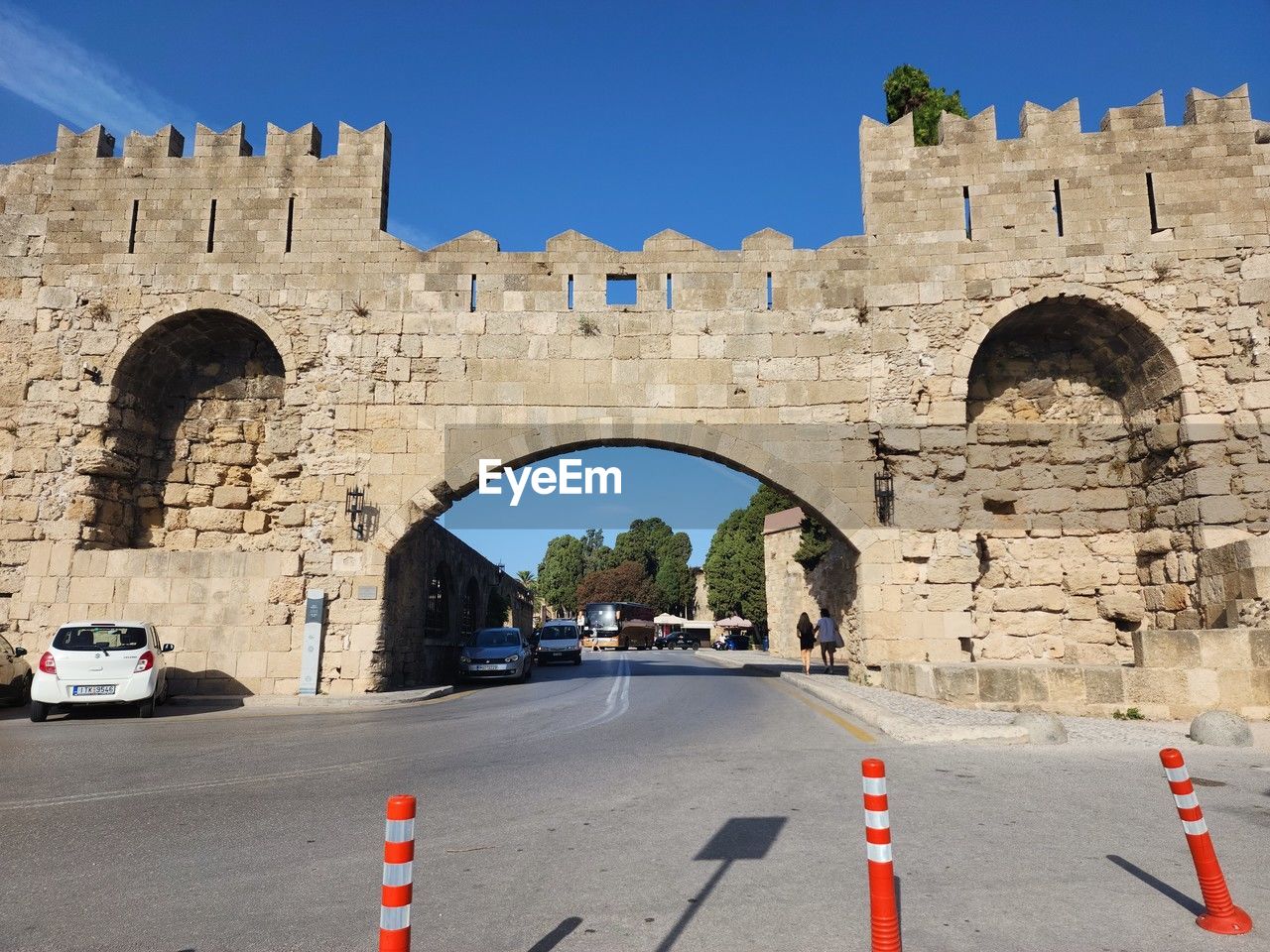 architecture, transportation, arch, built structure, history, city, the past, mode of transportation, road, travel destinations, motor vehicle, building exterior, car, travel, clear sky, nature, street, sky, day, sign, blue, ancient, sunny, outdoors, no people, sunlight, wall, symbol