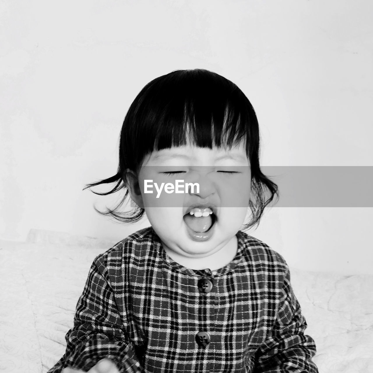 Close-up of cute baby girl with eyes closed and mouth open against white background