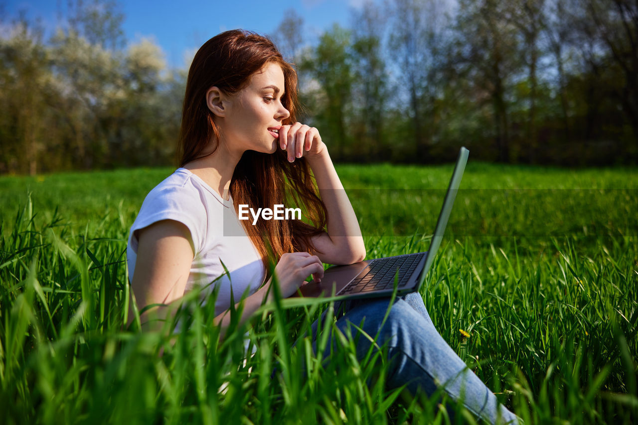 young woman using mobile phone while sitting on grassy field