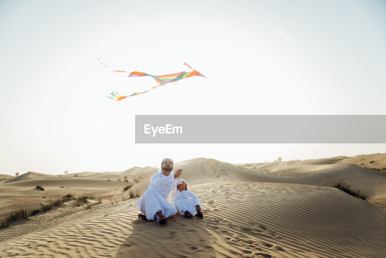 REAR VIEW OF PEOPLE SITTING ON SAND