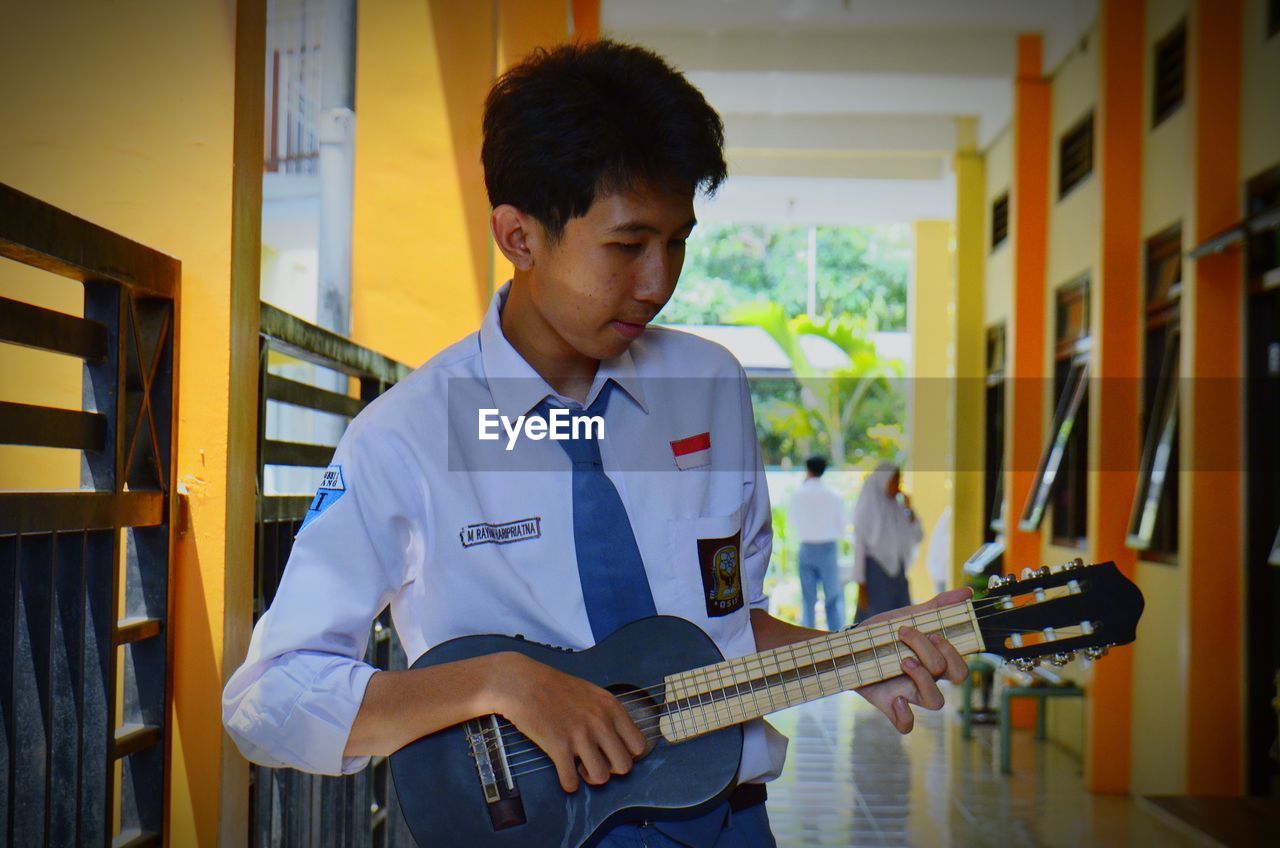 Young man playing guitar in corridor