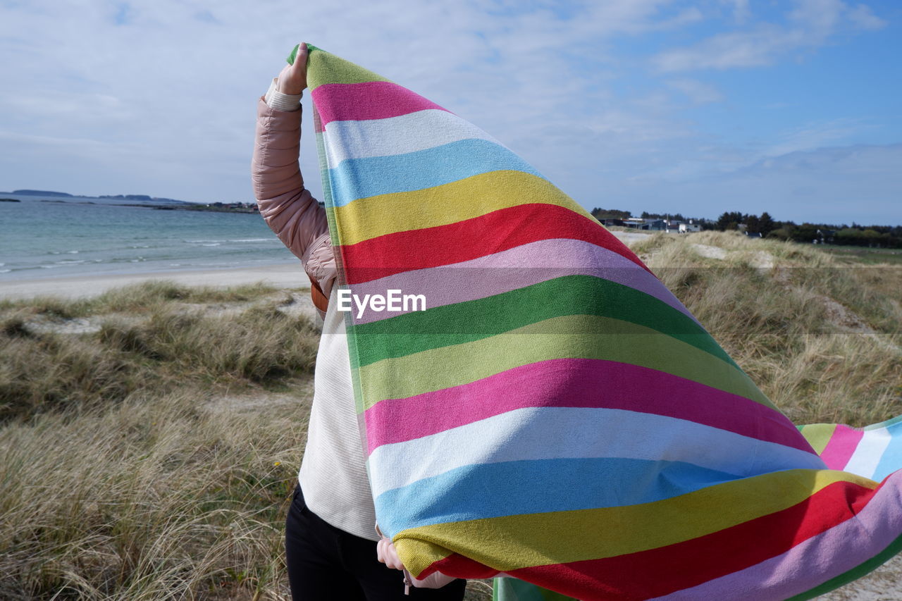 Low section of person holding towel on beach against sky