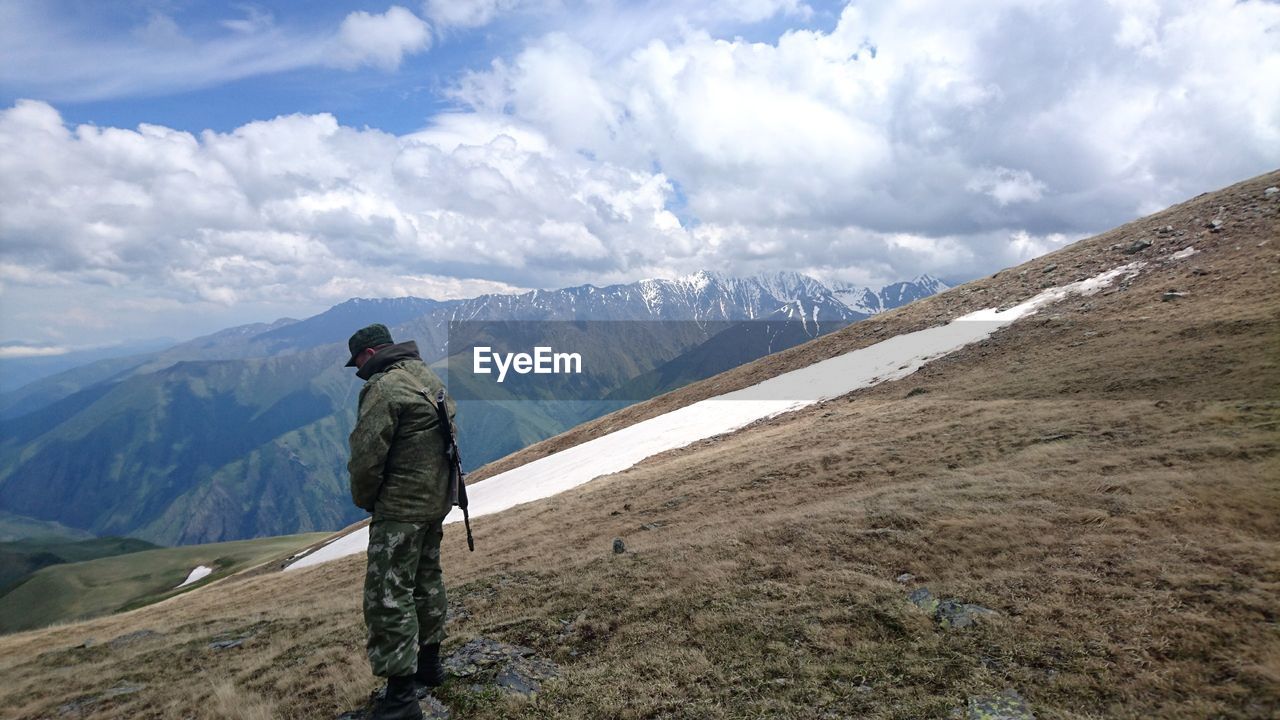 Side view of army officer standing on mountain against cloudy sky