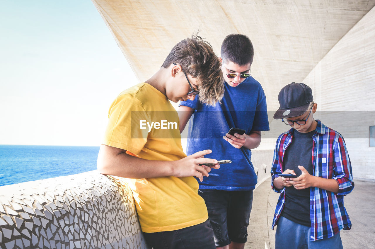 Friends using smart phones while standing by sea