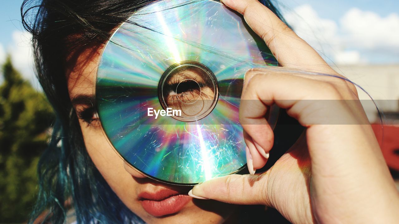 Young woman looking through hole of compact disk