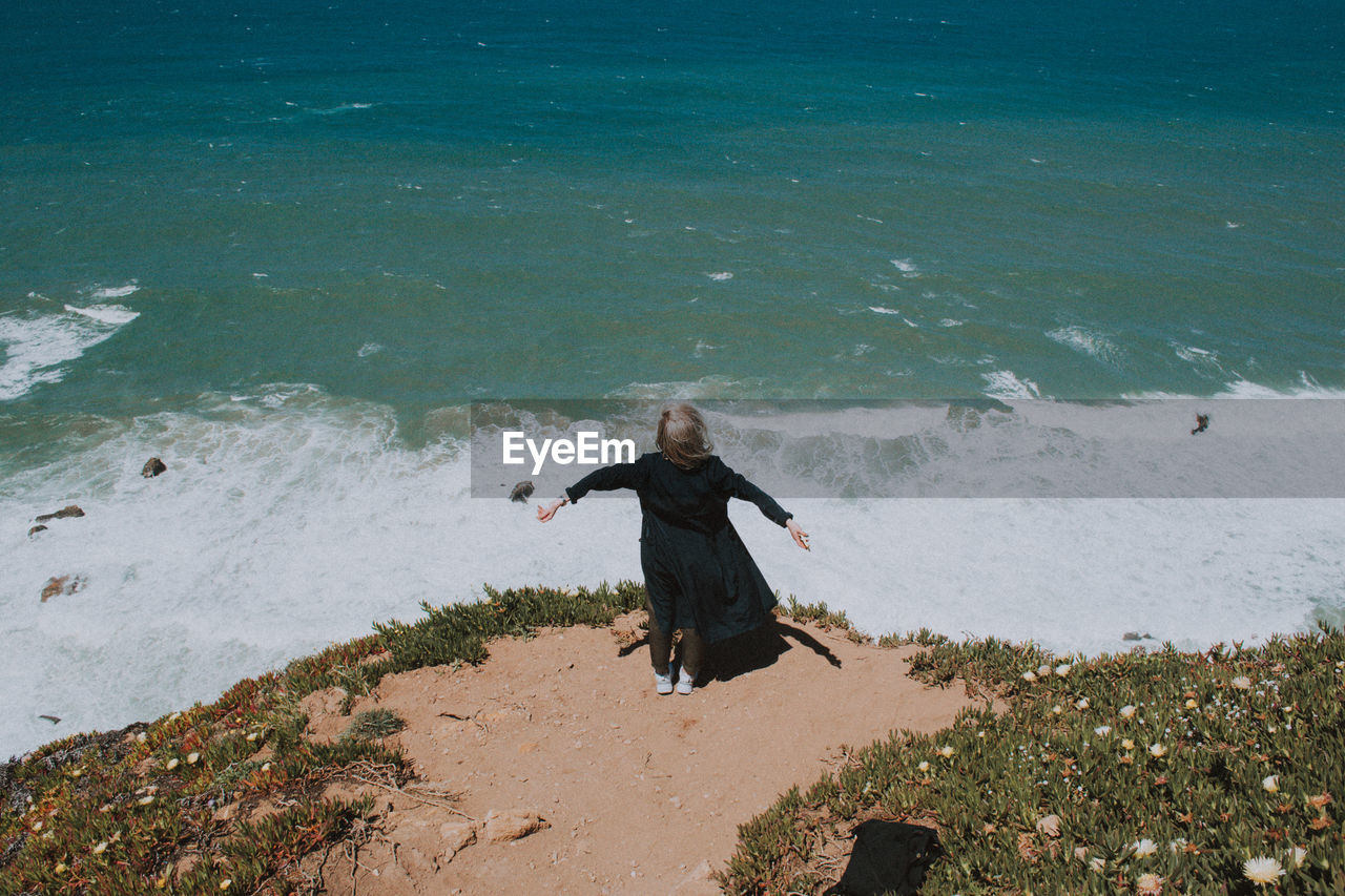 Rear view of woman standing on cliff by sea