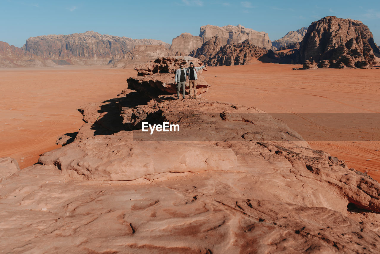 Remote view of male tourists standing on rocky formation in wadi rum valley and enjoying vacation in jordan