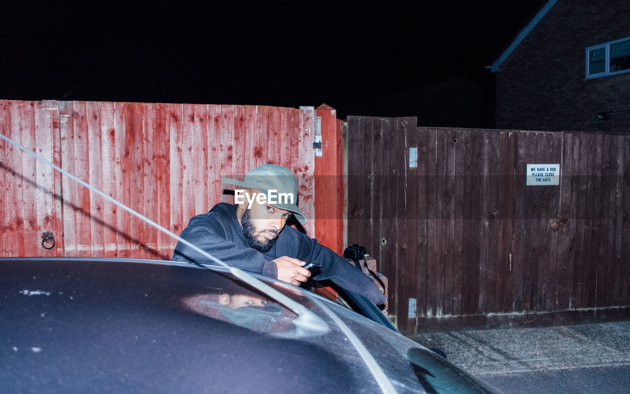 Portrait of man standing by car at night