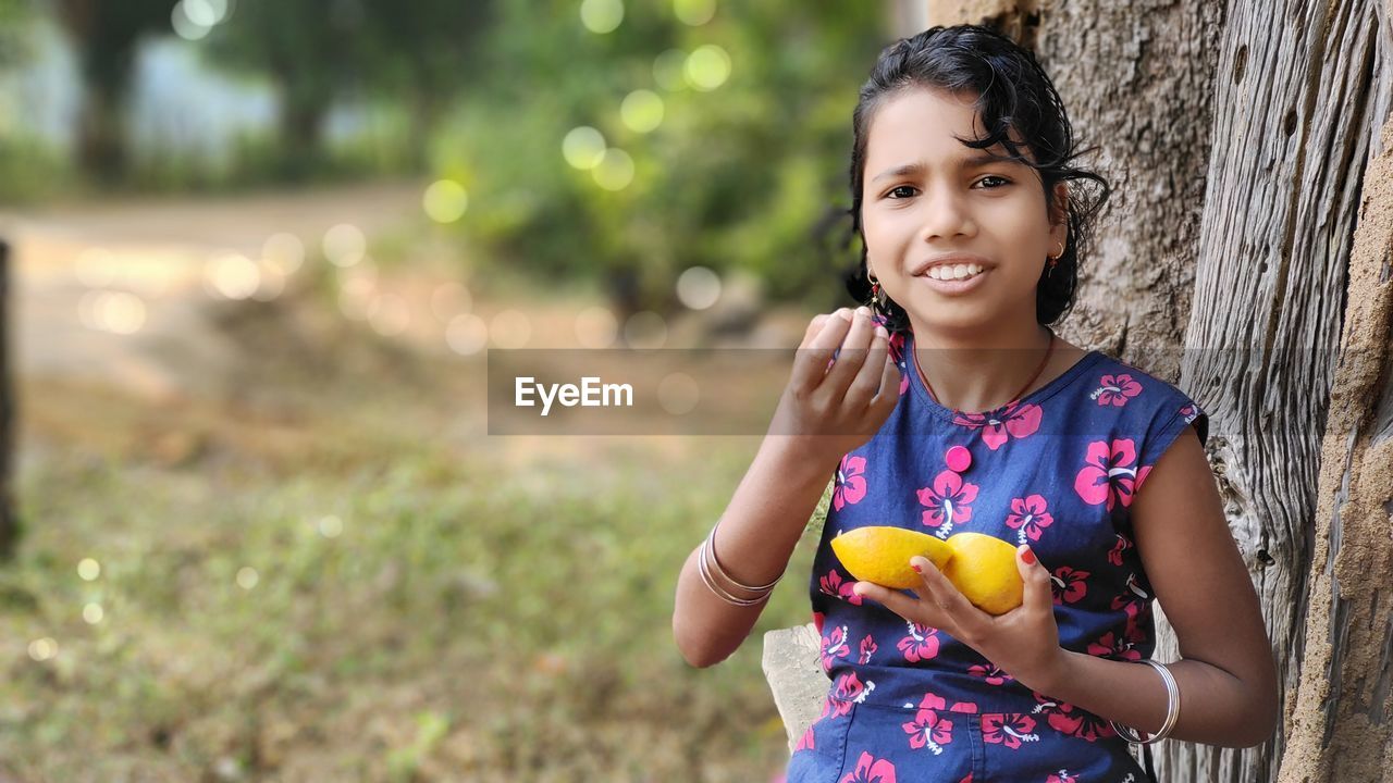 Little girl playing with fresh orange. blurred green background, copy space