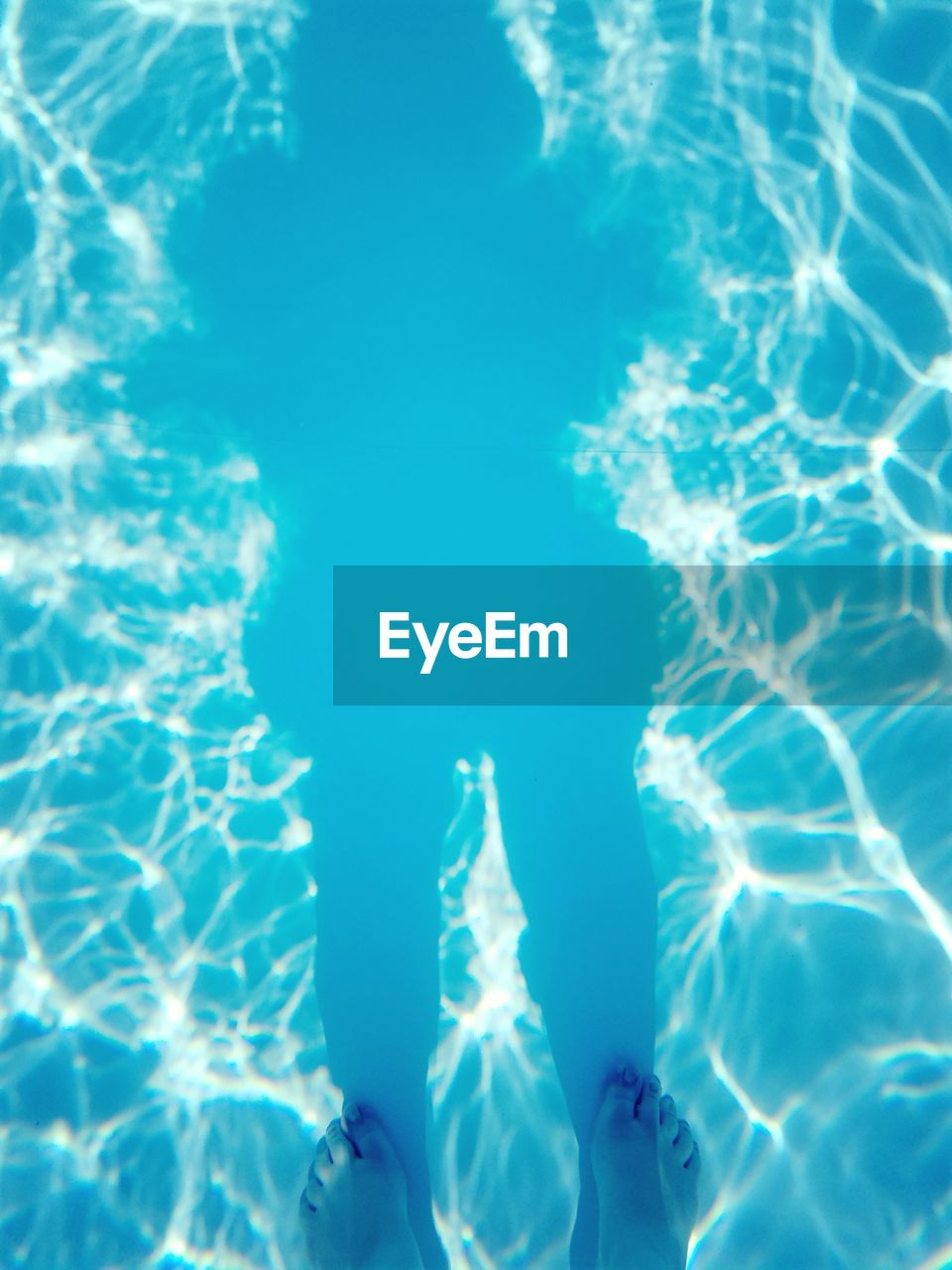 Low section of person with shadow standing on swimming pool