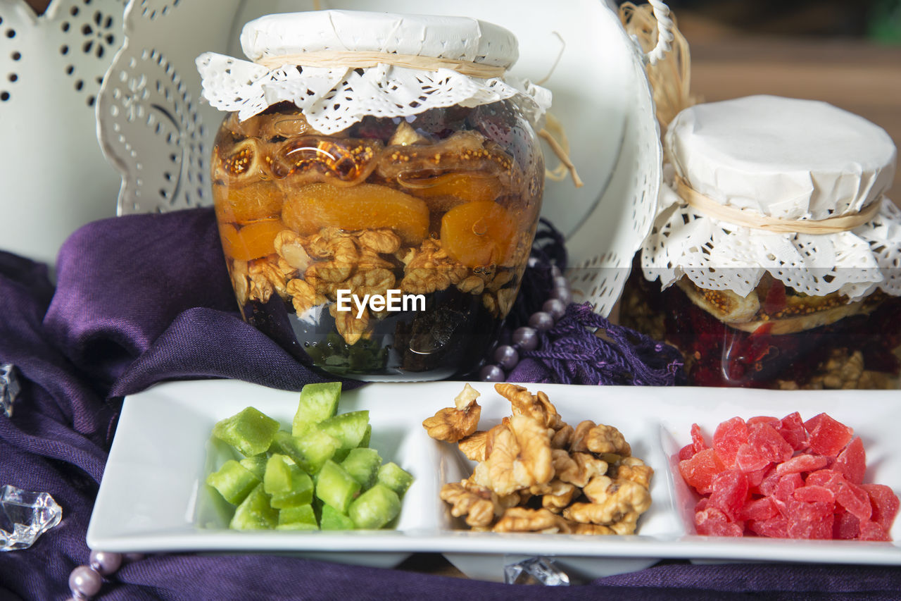Arrangement of walnut and dried fruit with honey topping in a jars and dried fruits in a bowl.