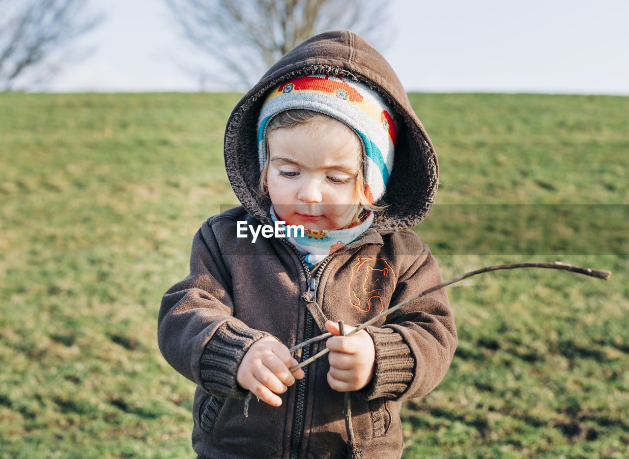 Cute girl holding stick while standing on grassy field against sky