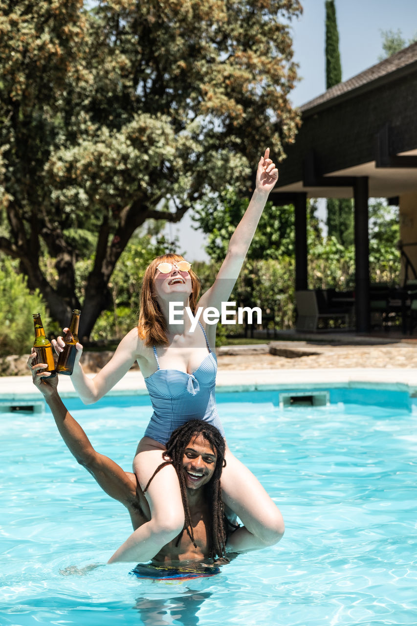 Happy man carrying girlfriend on shoulders in swimming pool