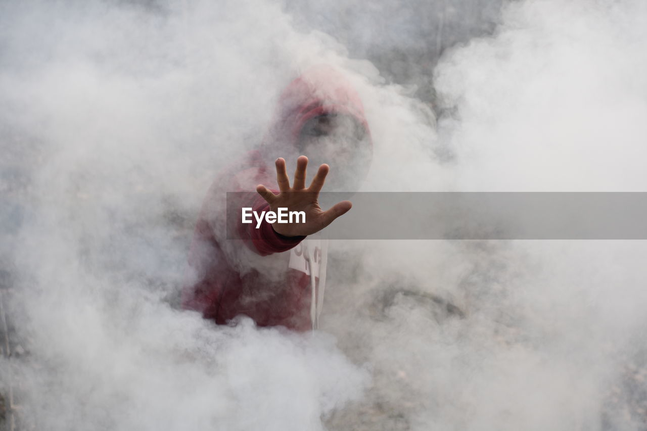 Man in hood standing amidst smoke