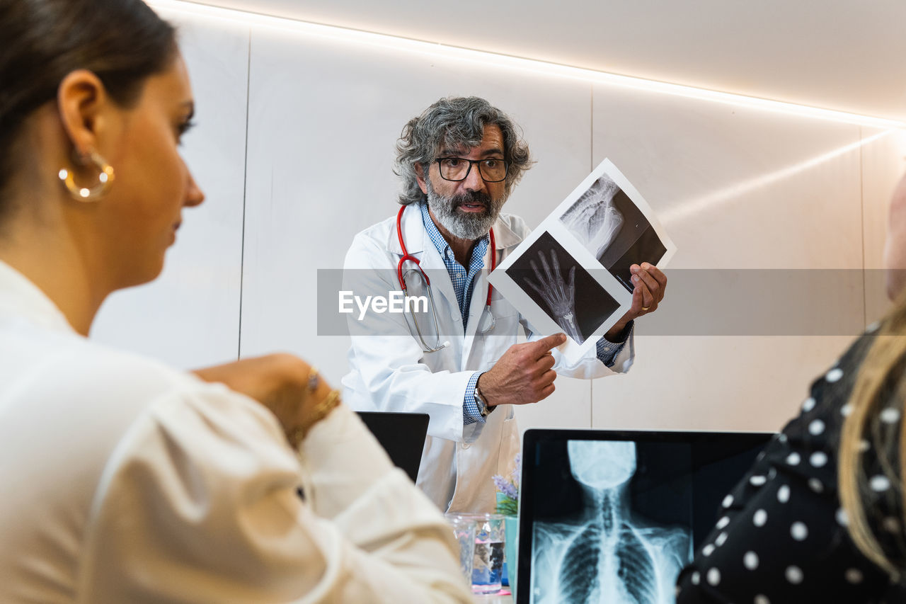 Elderly male medic explaining x ray image to coworkers while working in modern clinic