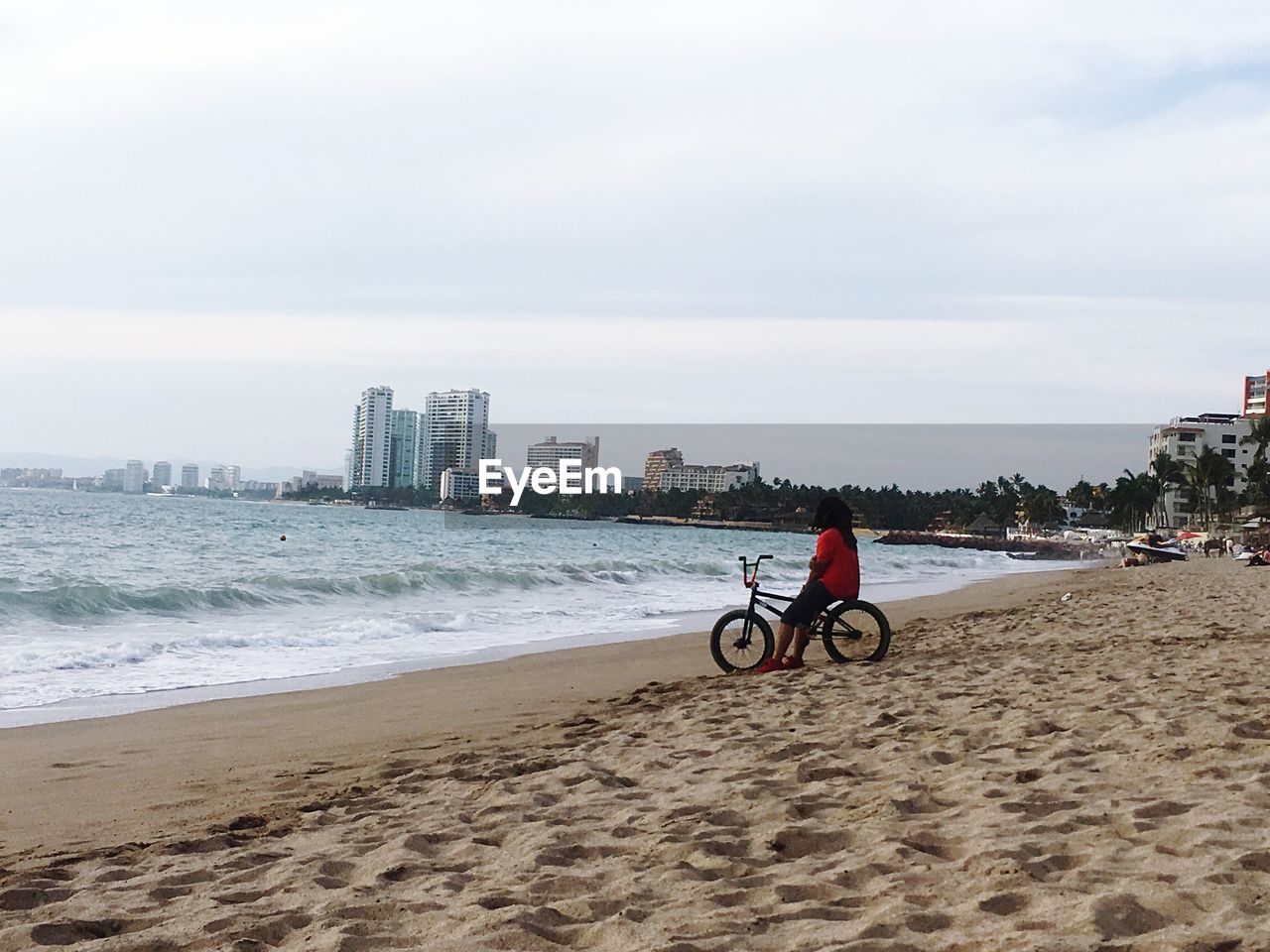 MAN WITH BICYCLE ON BEACH AGAINST SKY