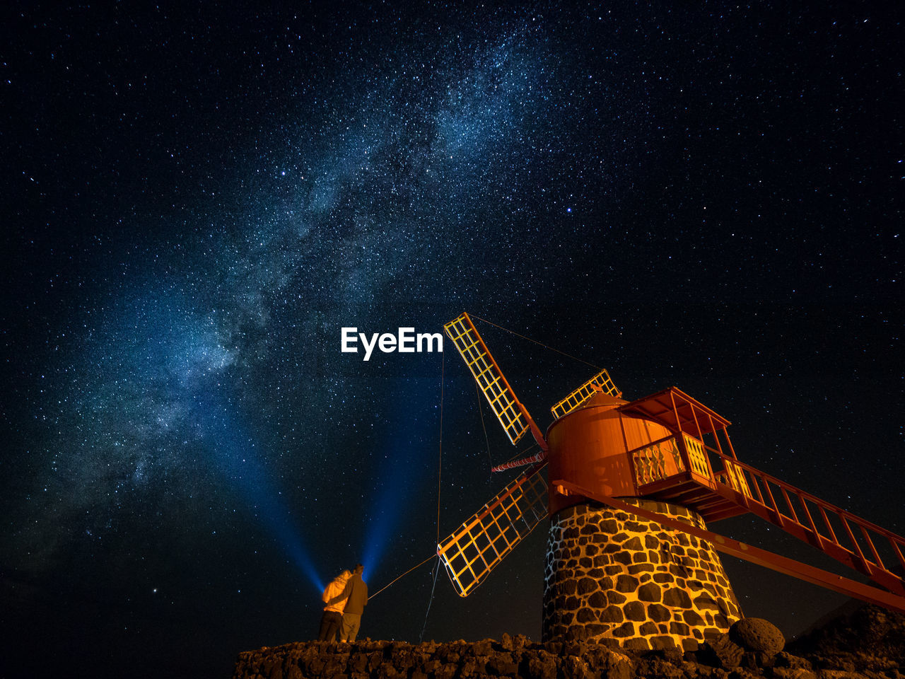 Low angle view of couple standing by windmill against star field at night
