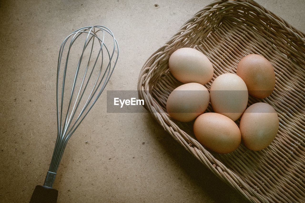 High angle view of eggs in tray by wire whisk on table