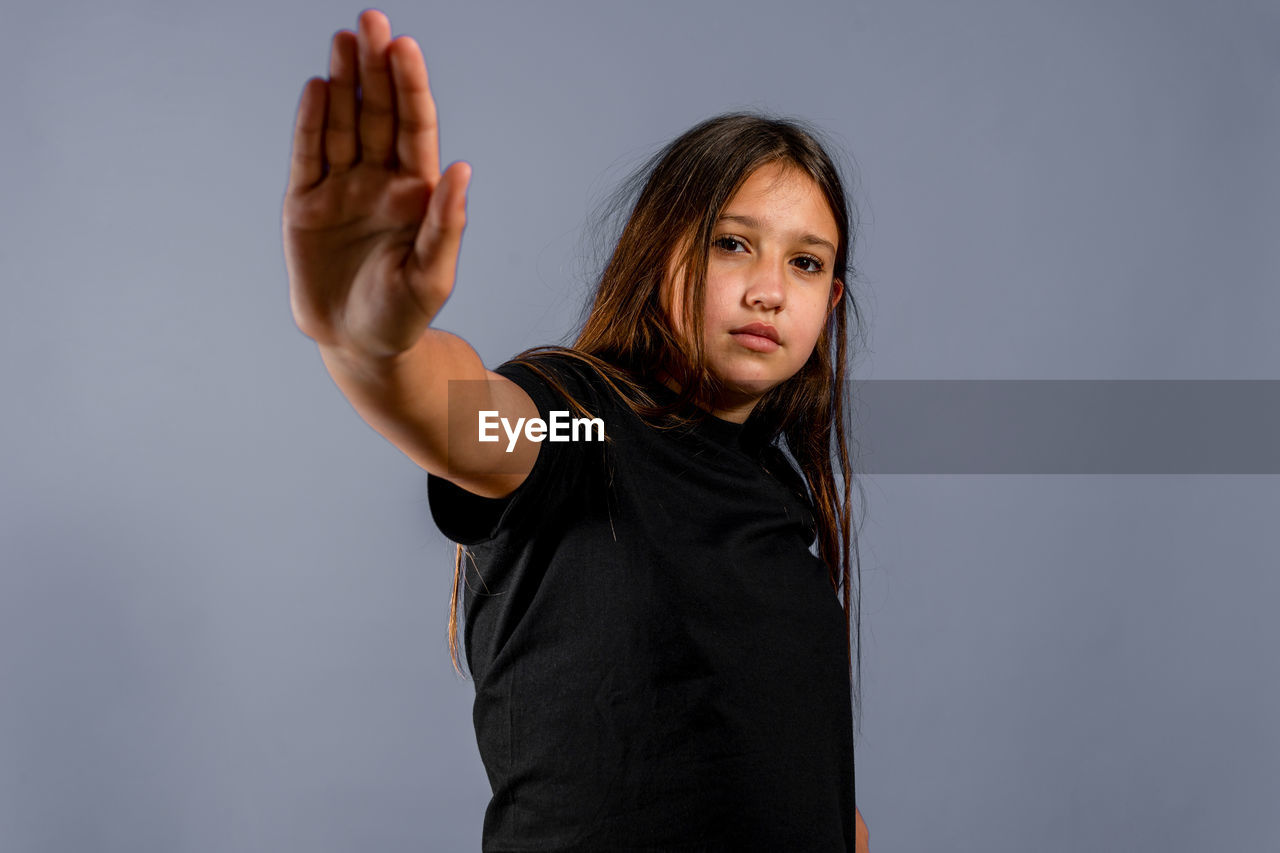 PORTRAIT OF GIRL STANDING AGAINST GRAY BACKGROUND