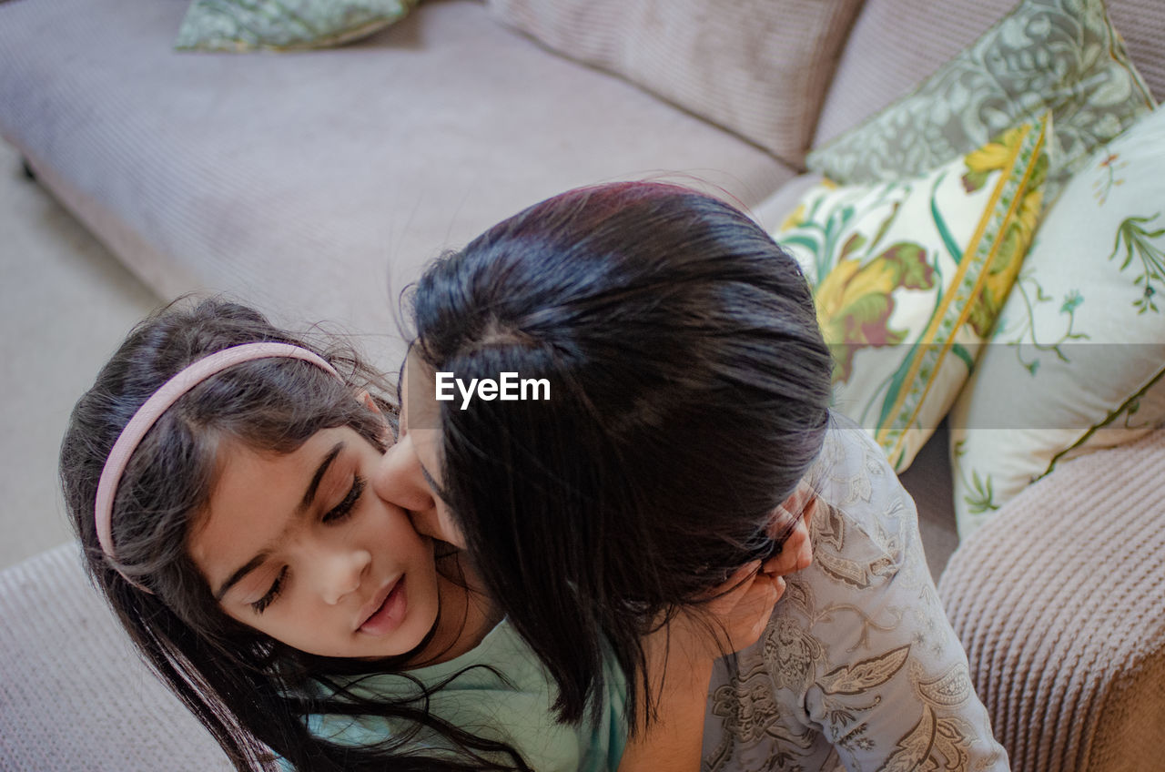 High angle view of woman kissing daughter on sofa at home