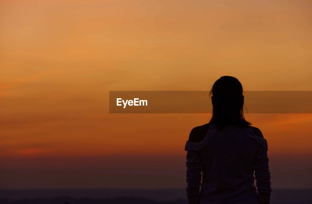 Rear view of woman standing against orange sky