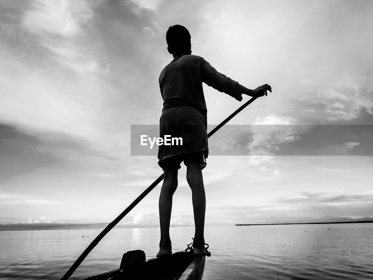 Rear view of boy on rowboat against sky