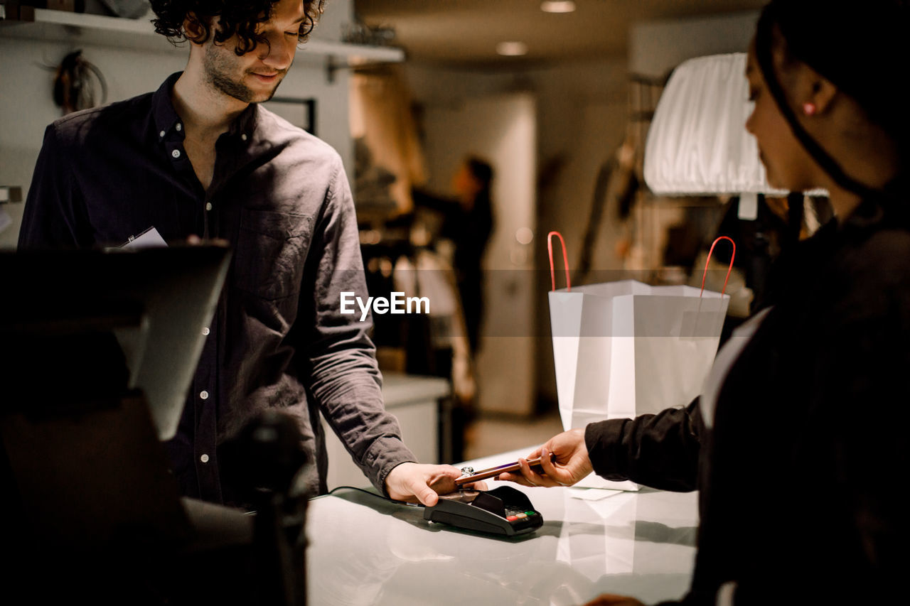 Side view of female customer paying through smart phone at store