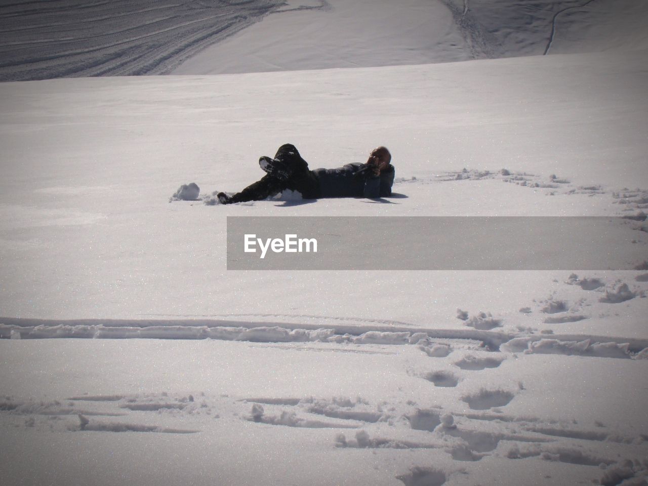 MAN LYING ON SNOW COVERED FIELD