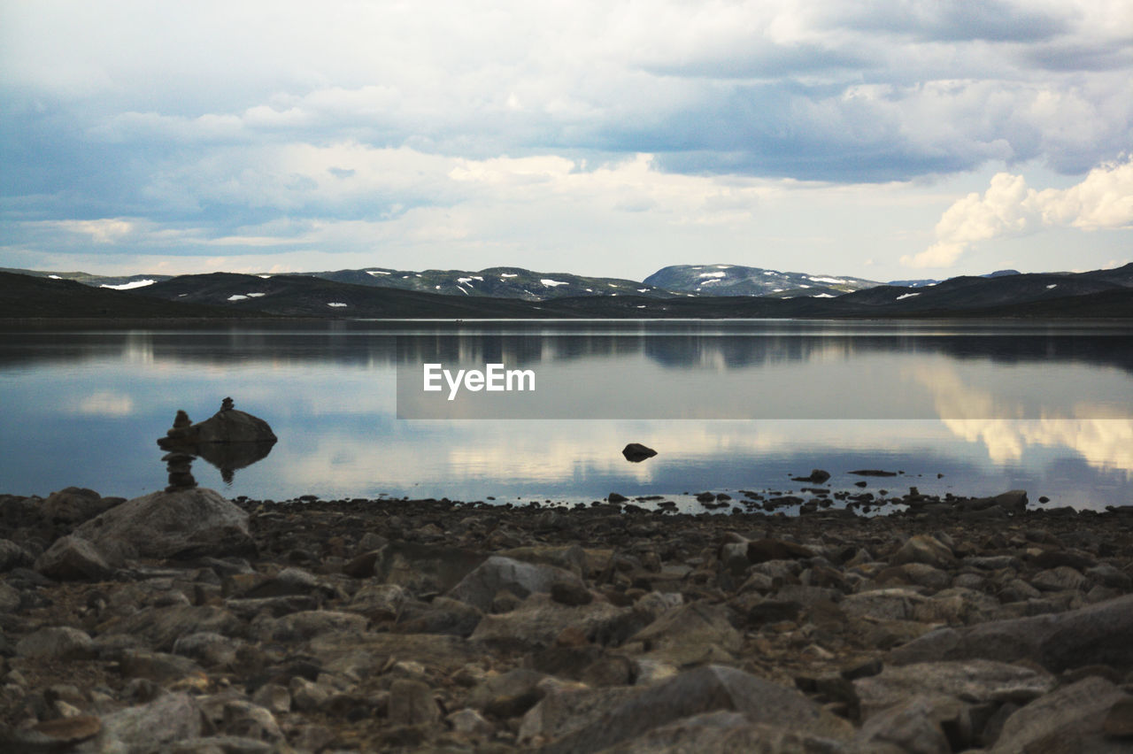 Scenic view of lake and field against cloudy sky