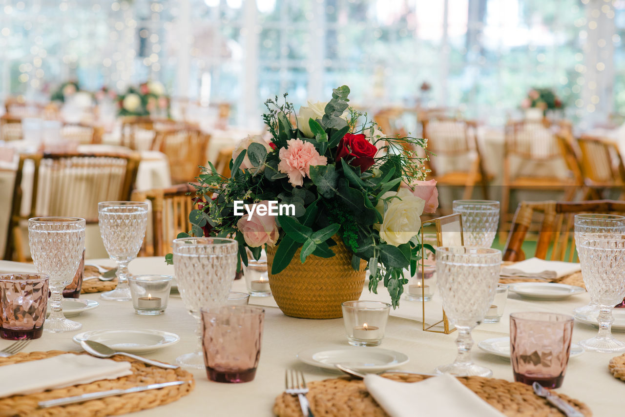 Simple unique flower bouquet in vase on festive decorated table with glassware in restaurant