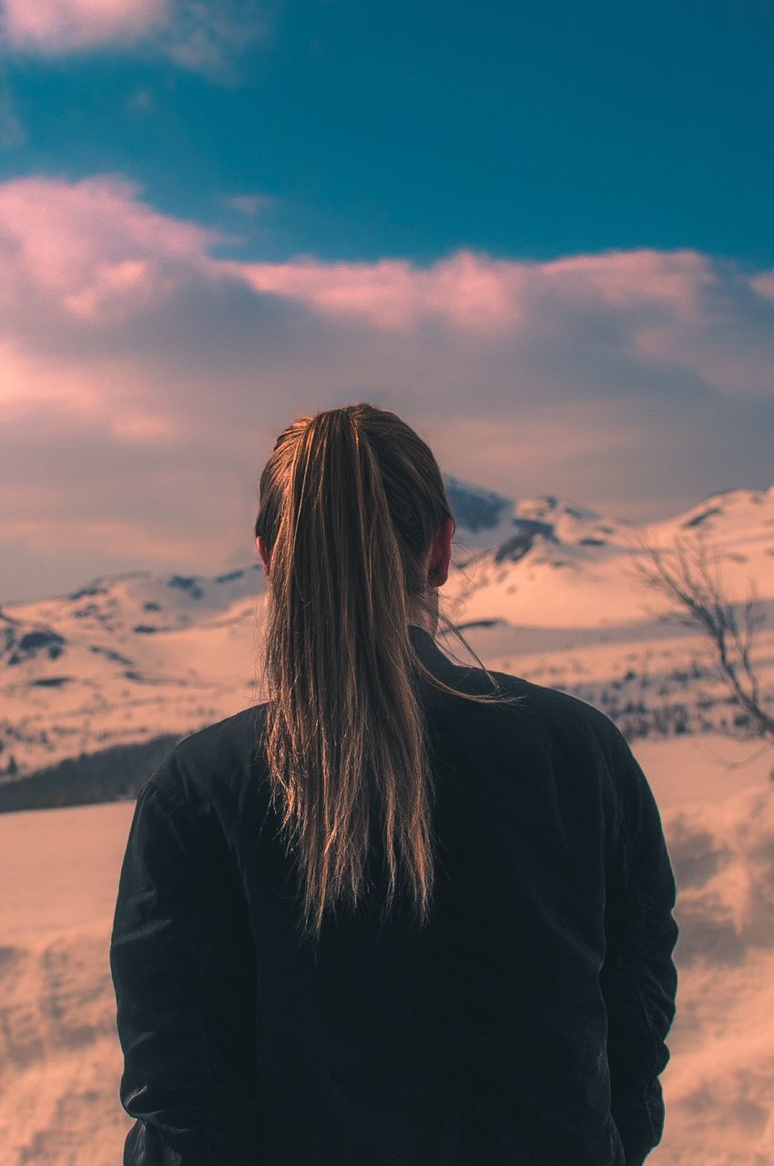 Rear view of woman on snow covered mountain standing against sky during sunset