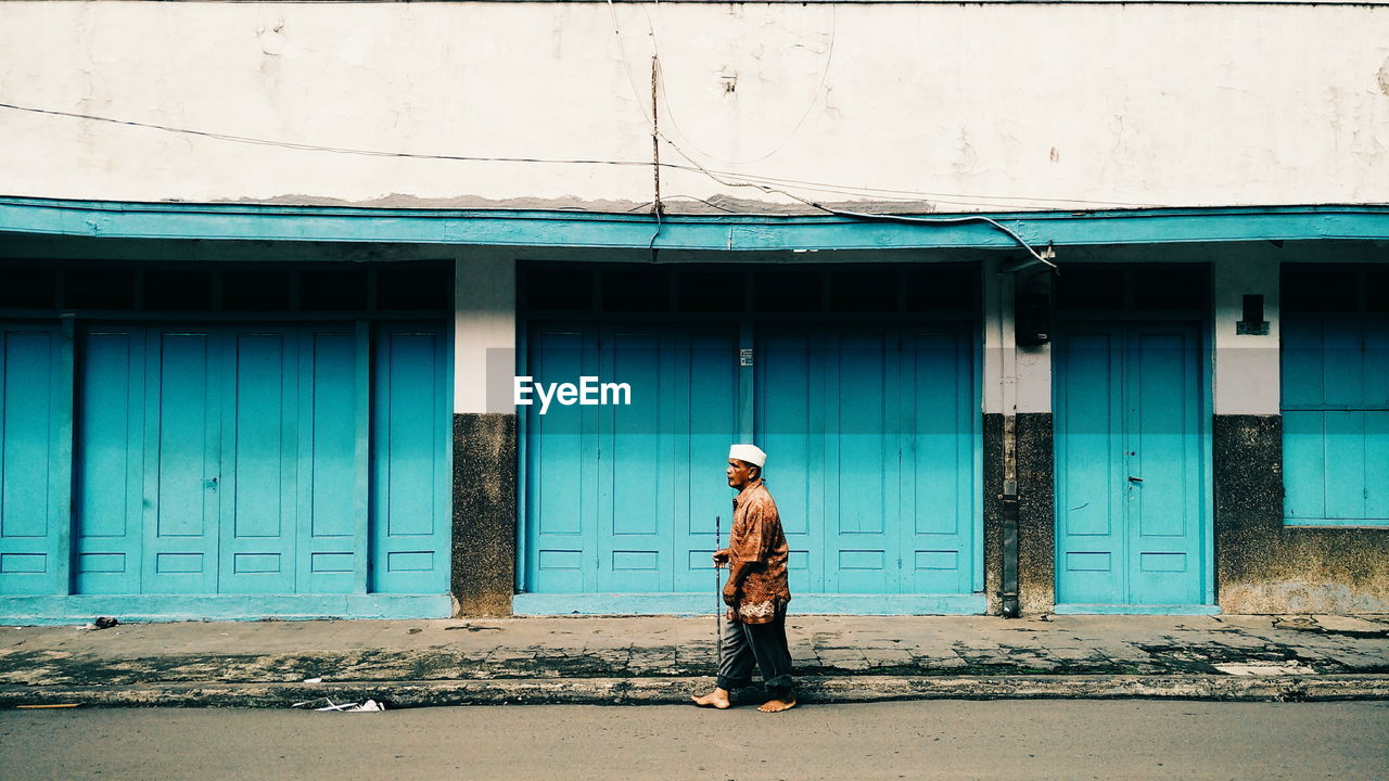 MAN STANDING BY STREET AGAINST BUILDING