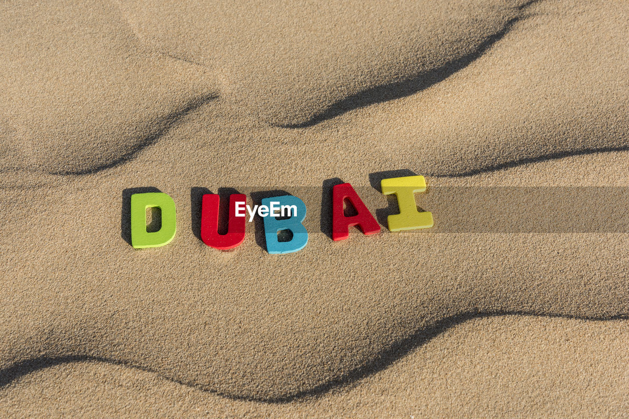Dubai word written with colorful letters on soft sand of the desert