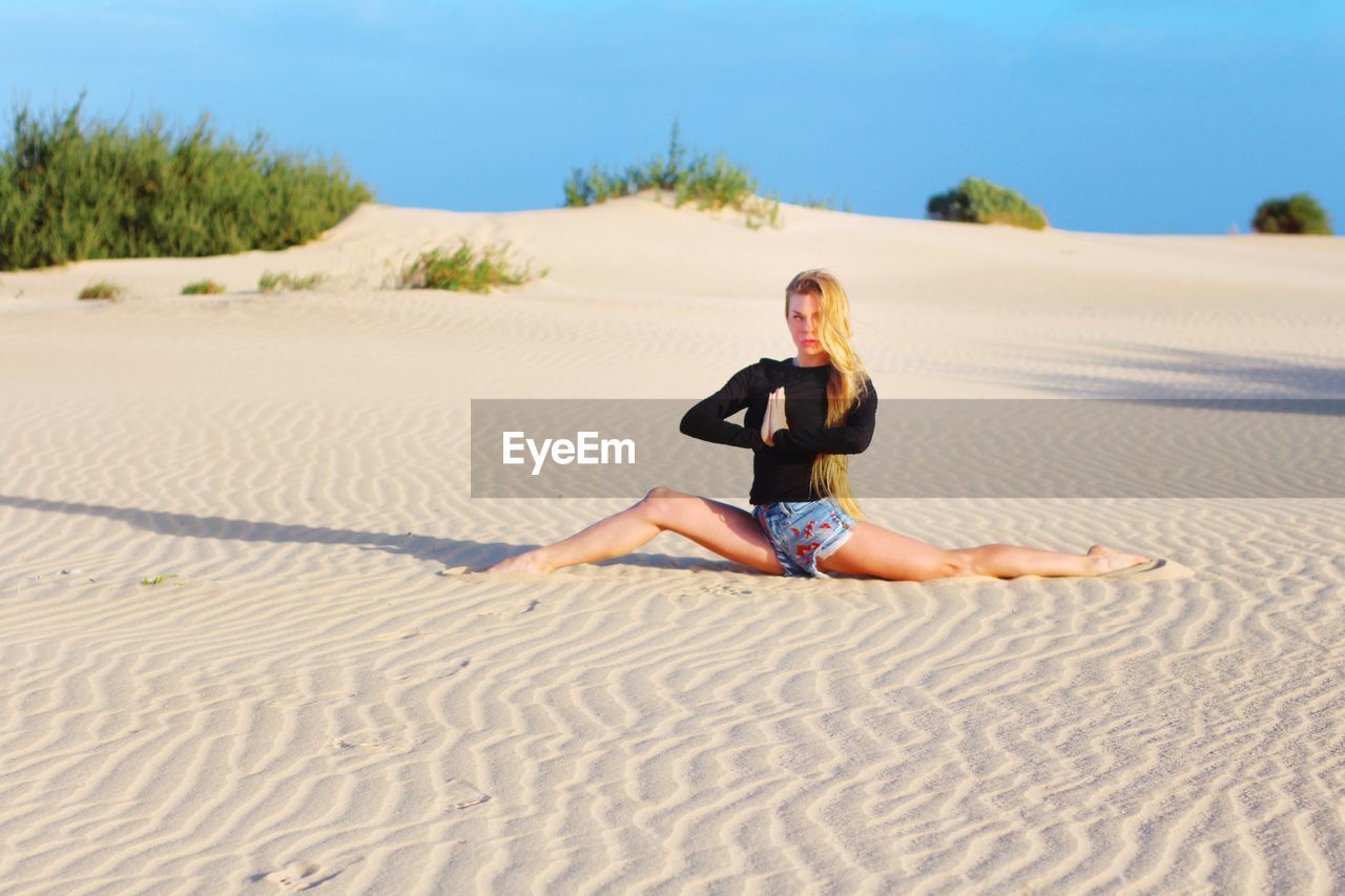 Full length of young woman doing yoga on sand at beach against sky