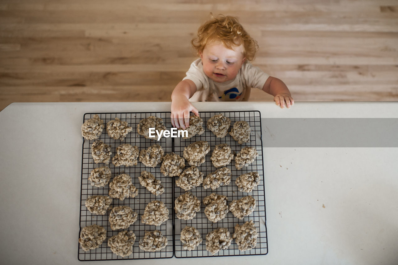 High angle view of cute baby boy taking cookies from table at home