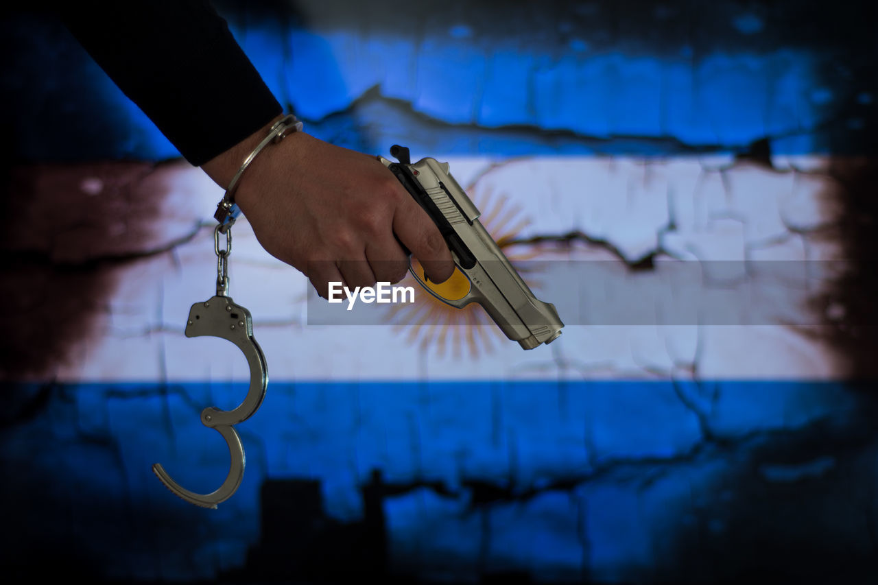 Cropped hand with handcuffs holding gun against argentinian flag