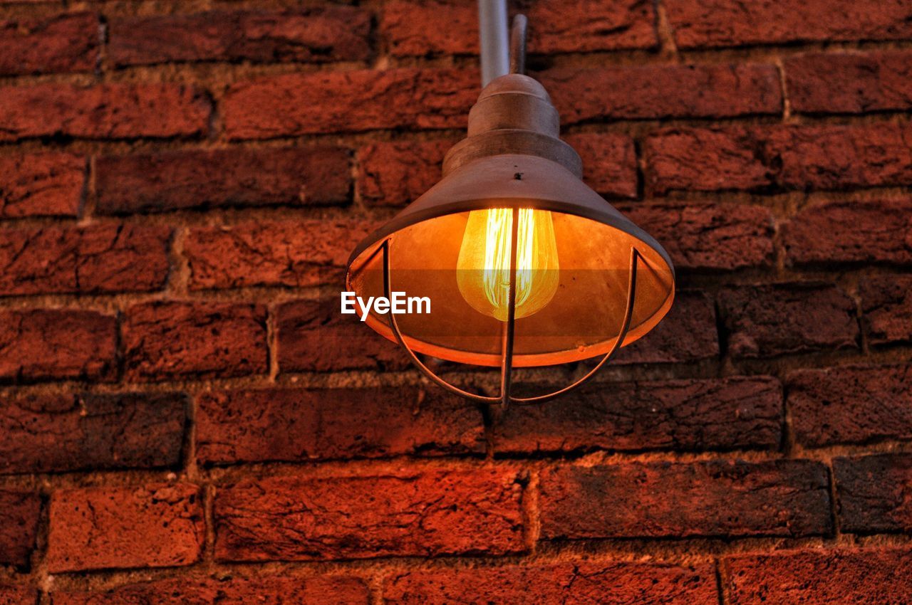 Low angle view of illuminated lamp against brick wall