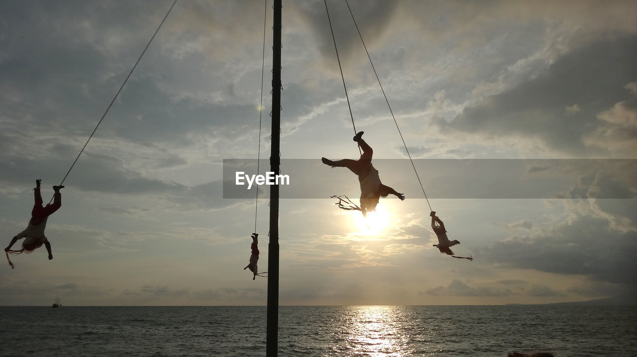 People hanging over sea against cloudy sky during sunset