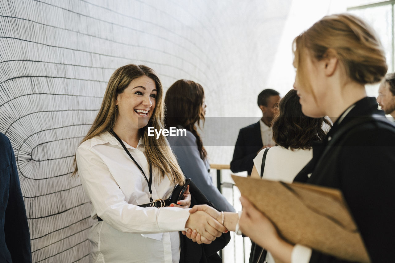 Happy pregnant female entrepreneur greeting businesswoman while doing handshake during networking event