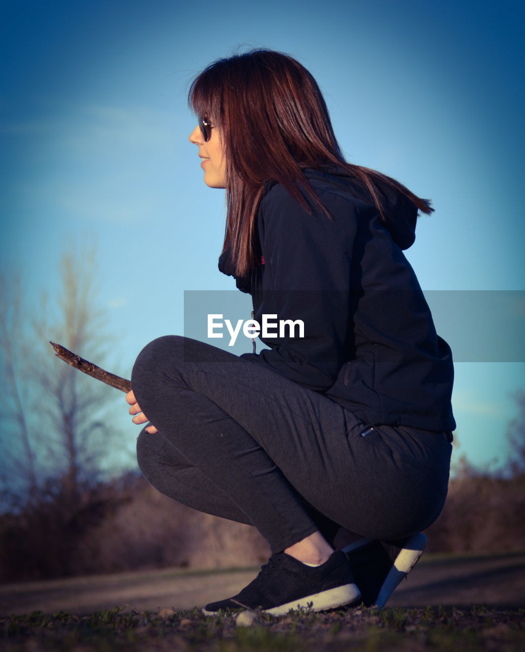 Side view of woman crouching on field against clear sky