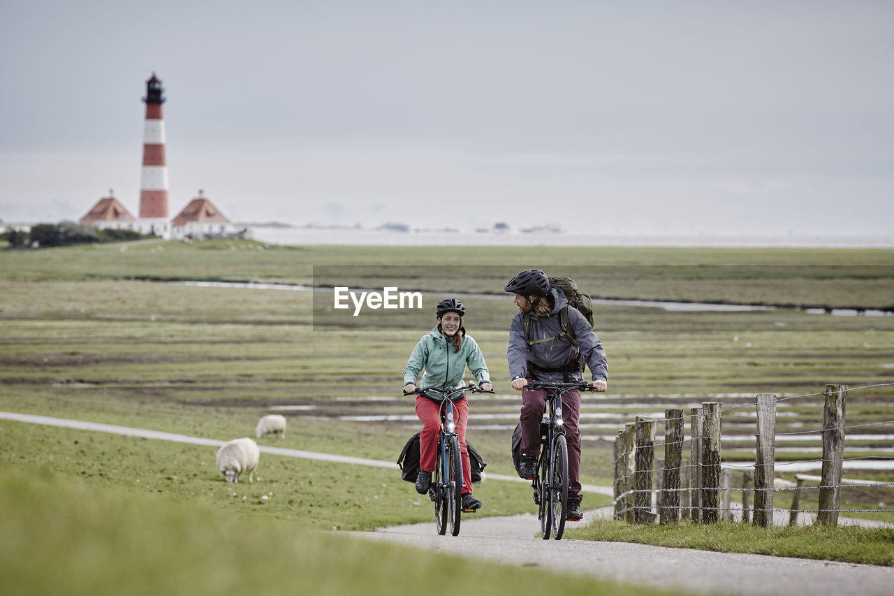 Germany, schleswig-holstein, eiderstedt, couple riding bicycle near westerheversand lighthouse