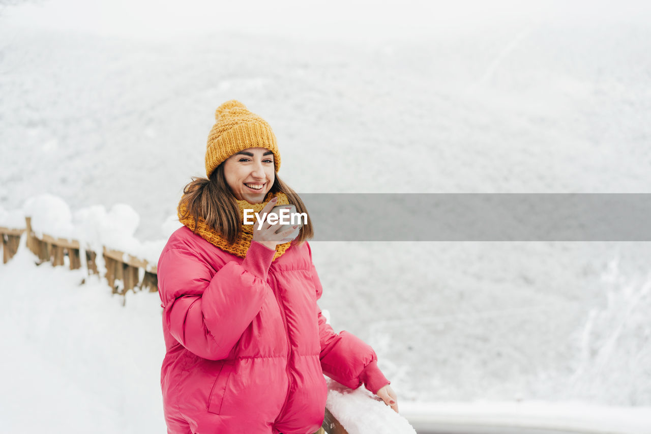 Happy woman in a landscape of winter snowy mountains laughs and drinks tea.