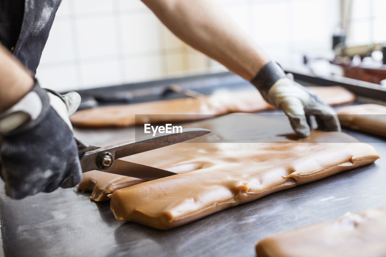 Cropped image of worker cutting caramel with scissors in candy store
