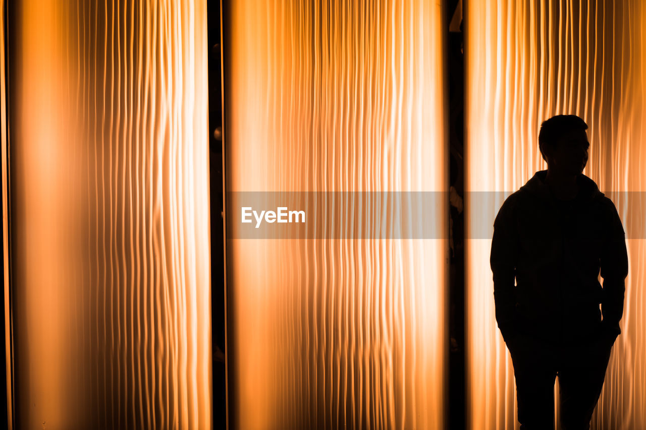 Silhouette man standing against illuminated curtain