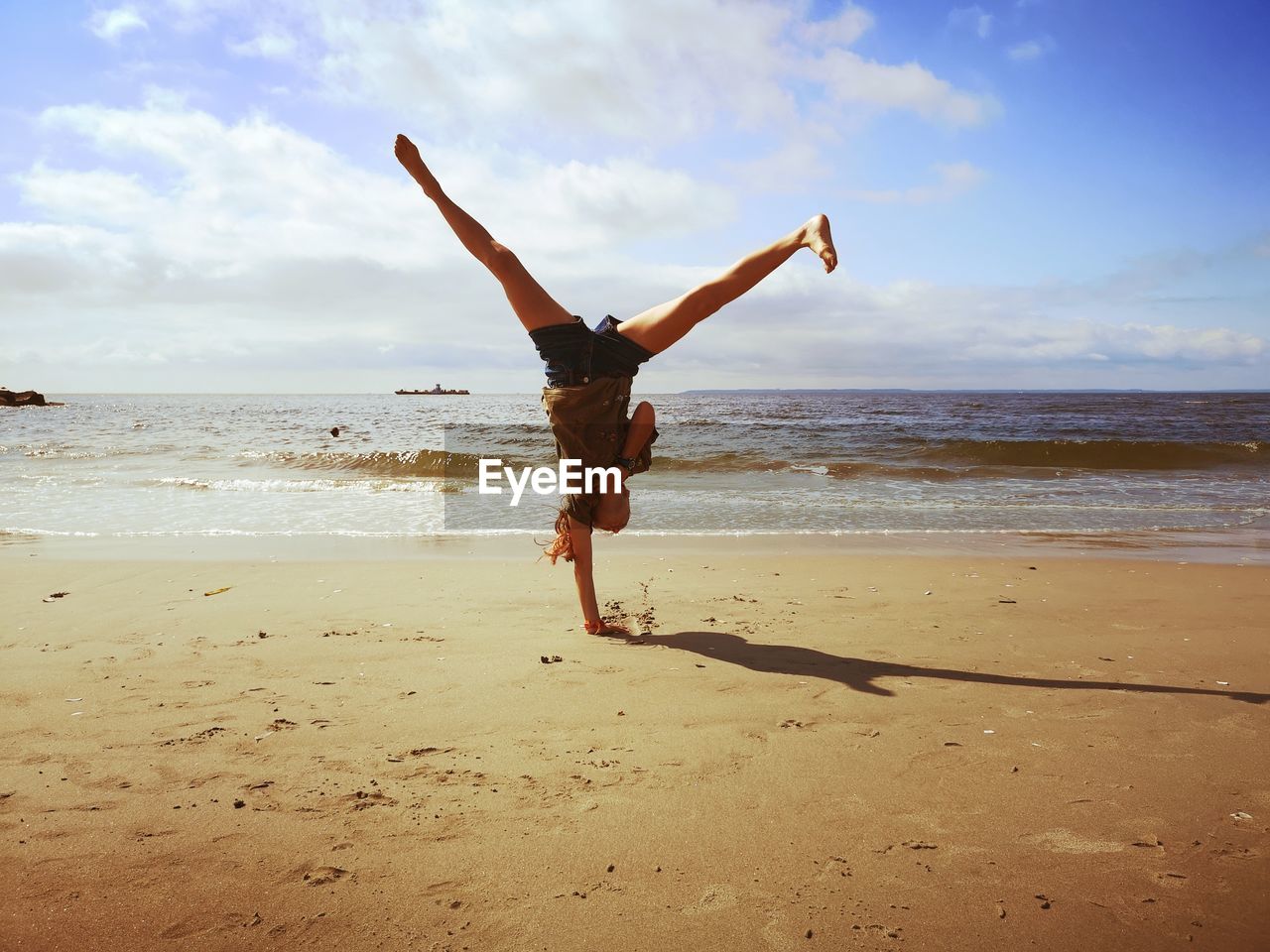 Full length of woman practicing handstand at beach against sky