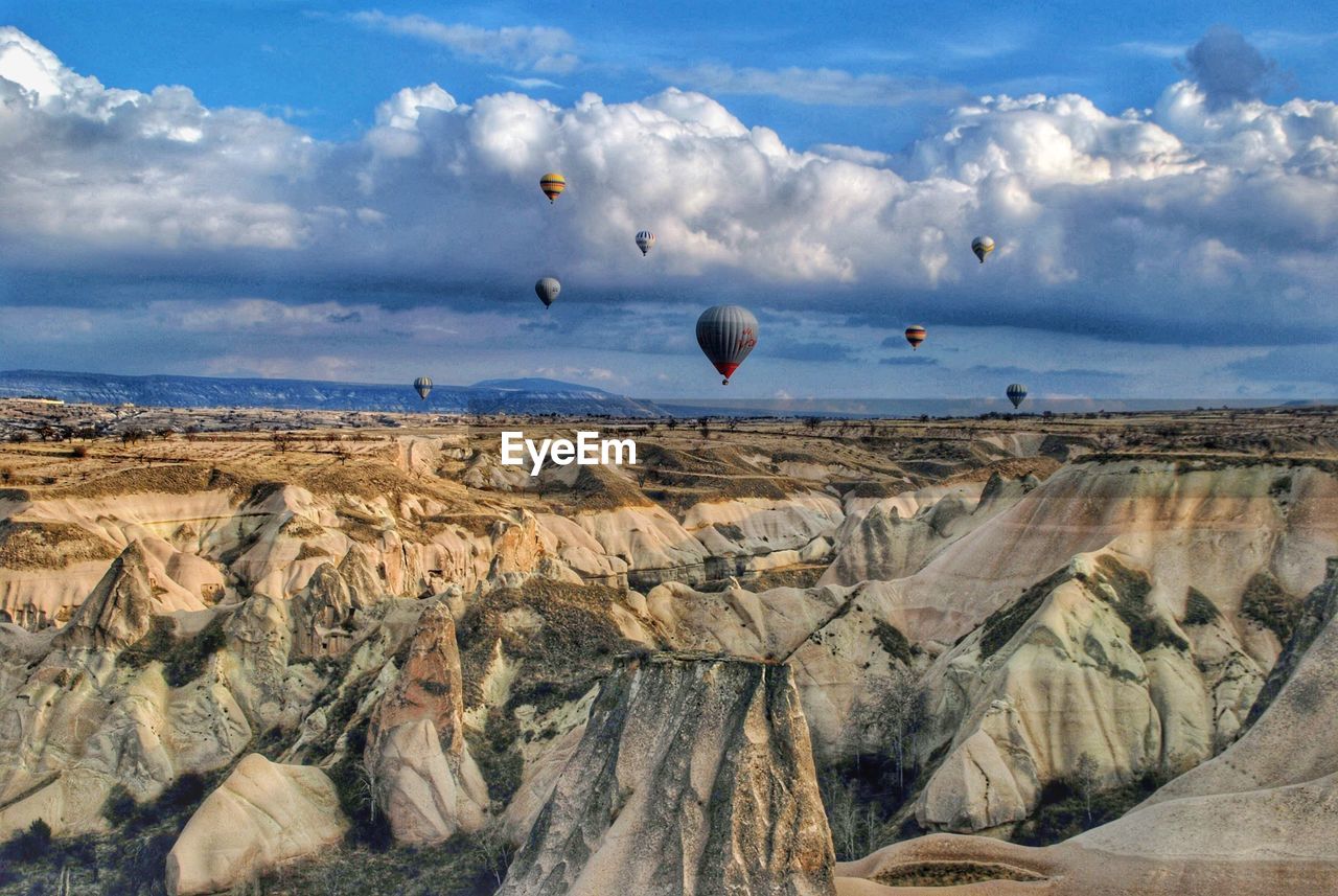 Hot air balloons flying over rock formation against sky