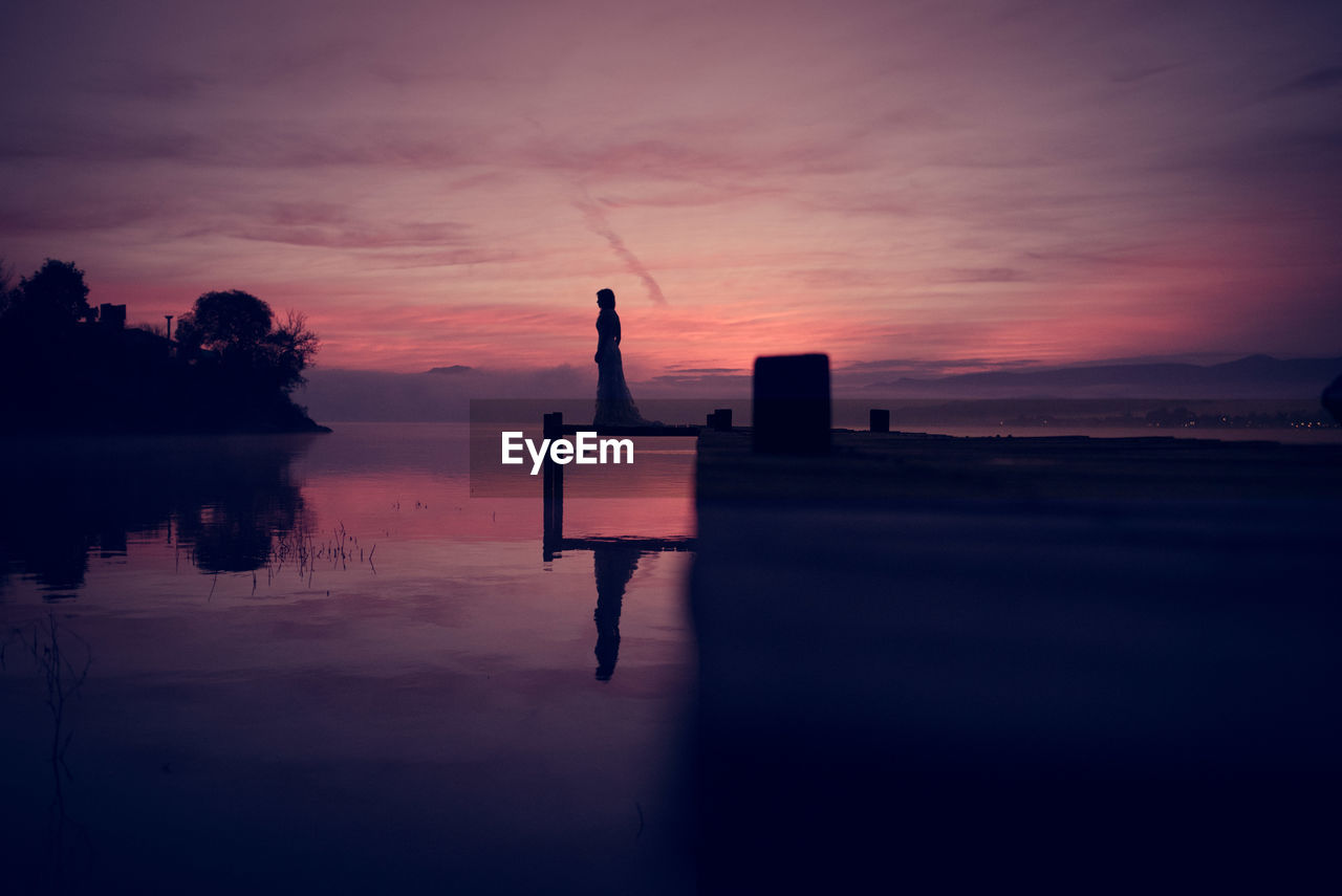 Silhouette model standing on pier in sea against cloudy sky
