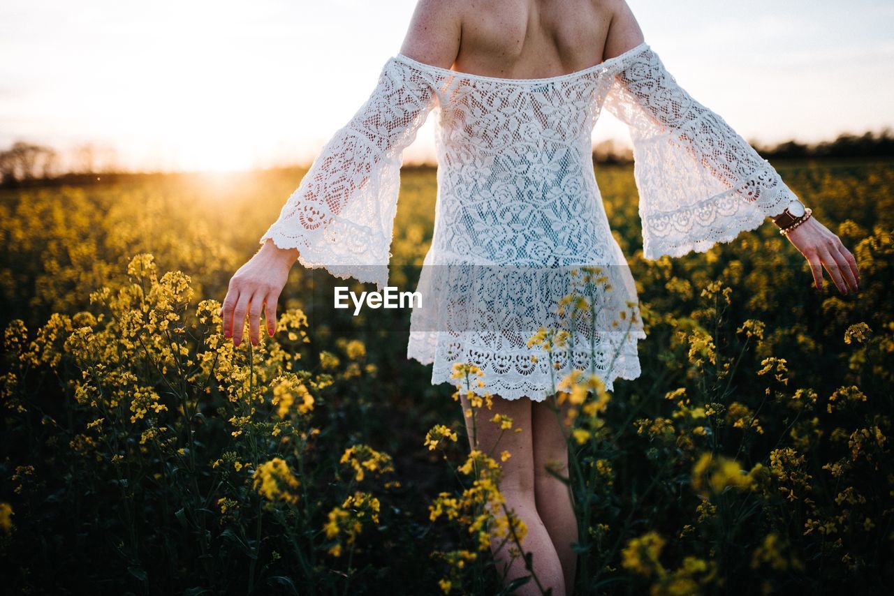 Midsection of woman standing amidst flowers against sky during sunset