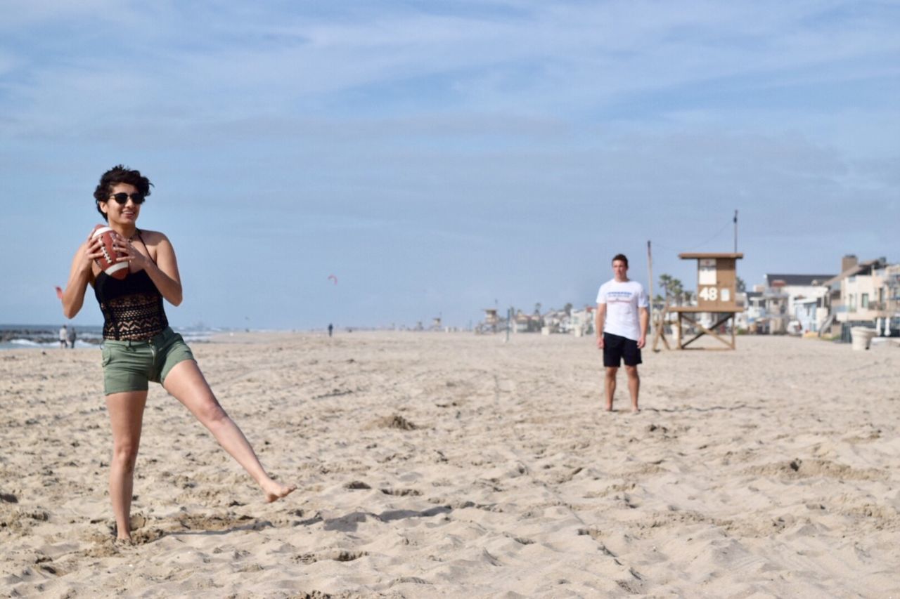 Woman playing with rugby ball at beach against sky