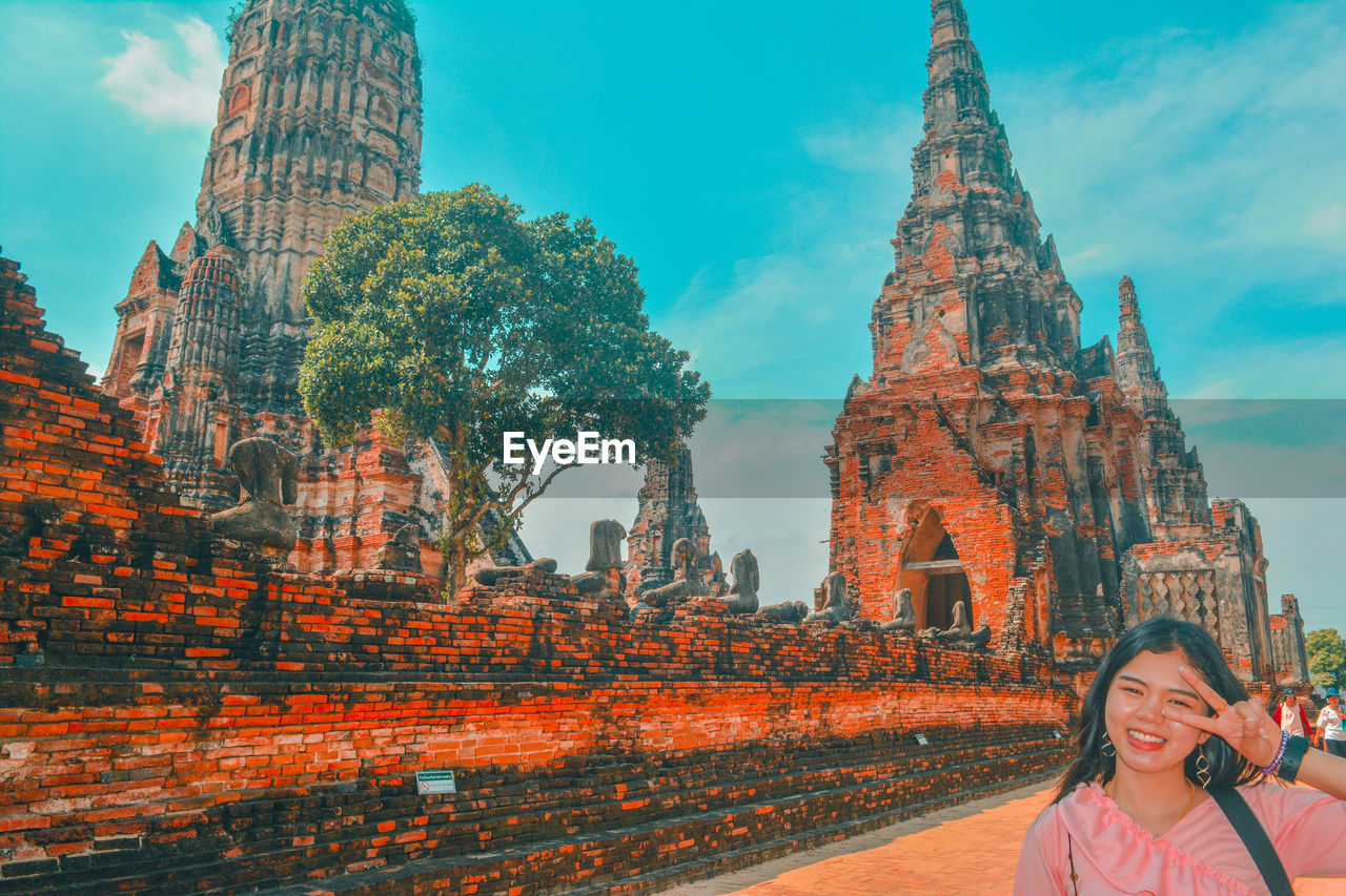 Portrait of smiling young woman standing against built structure